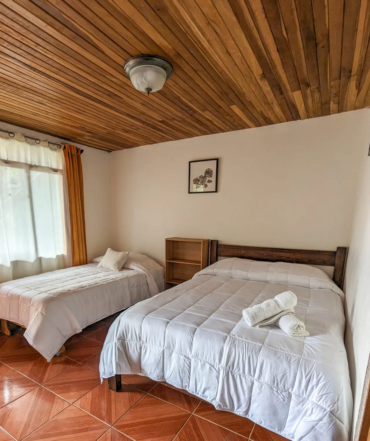 Habitación con cama matrimonial y cama individual y cielo raso de madera