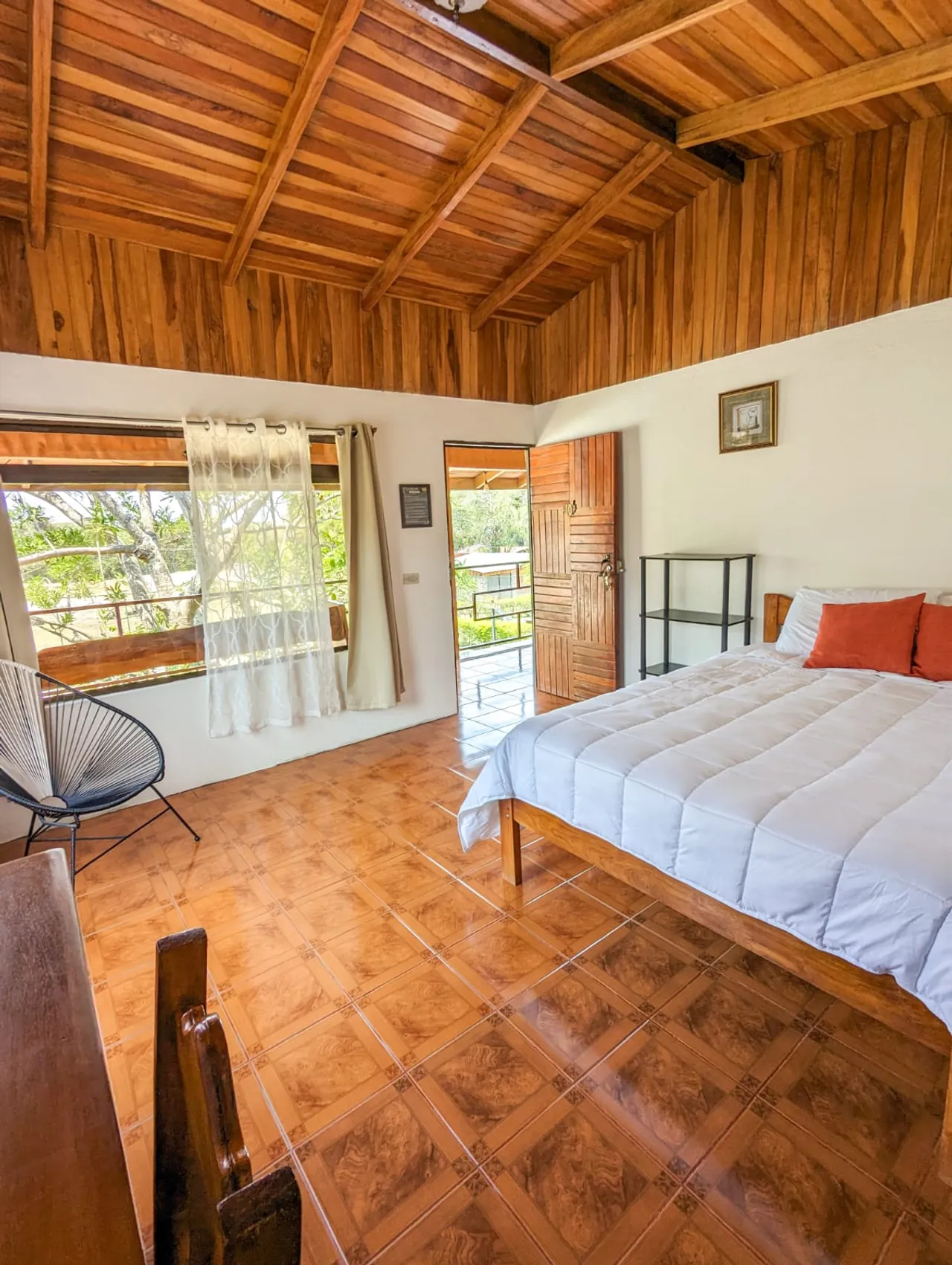 Habitación iluminada con cama matrimonial, techo de madera y vista al jardín