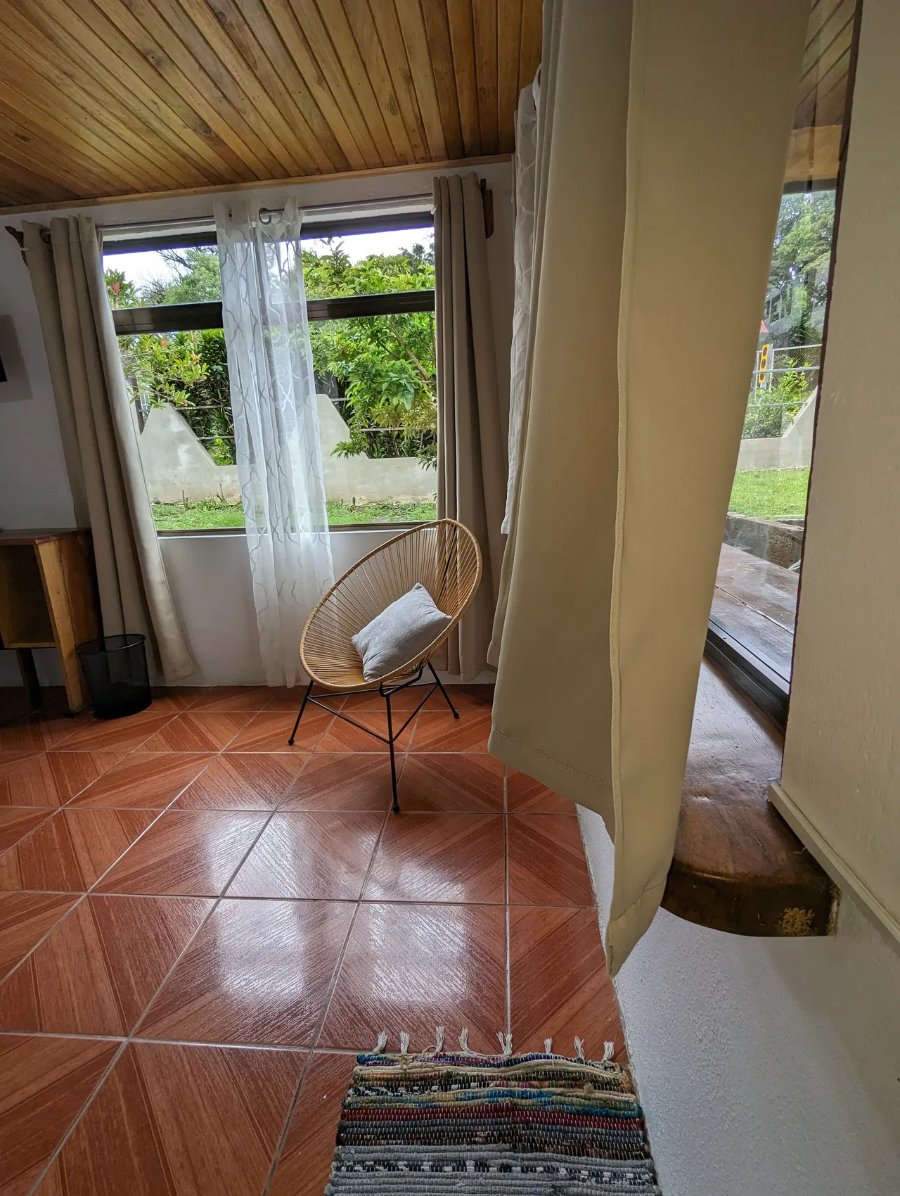 Habitación iluminada con silla acapulco y ventana al jardín